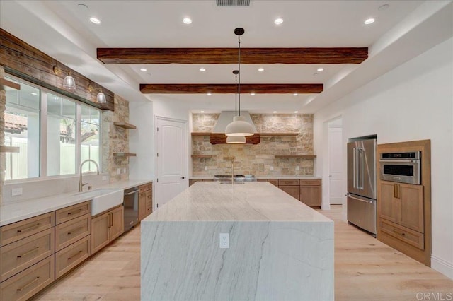 kitchen featuring sink, decorative light fixtures, light hardwood / wood-style flooring, appliances with stainless steel finishes, and a large island