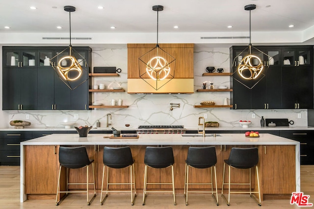 kitchen featuring a center island with sink, pendant lighting, light wood-type flooring, and sink