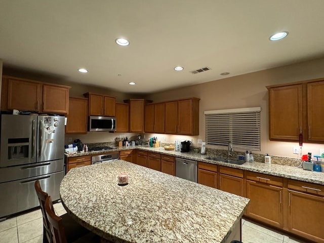 kitchen featuring light stone countertops, sink, stainless steel appliances, a kitchen island, and light tile patterned flooring