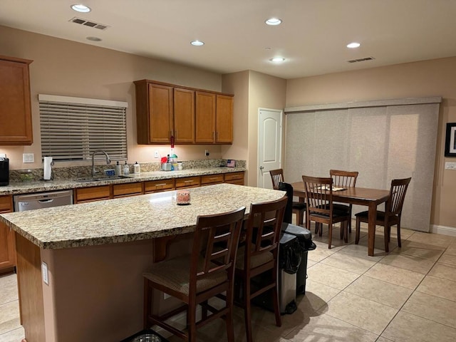 kitchen with sink, light tile patterned floors, light stone counters, stainless steel dishwasher, and a kitchen island