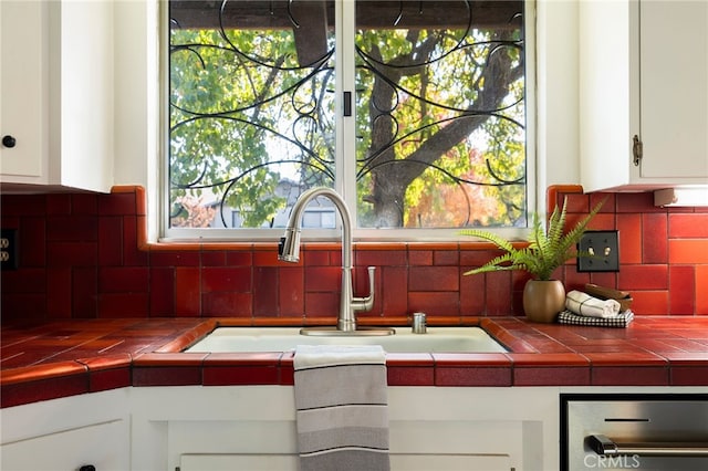 interior details featuring white cabinetry, tile counters, sink, and decorative backsplash