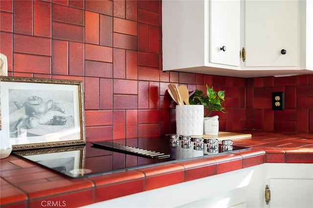 details with white cabinetry, decorative backsplash, tile counters, and black electric cooktop