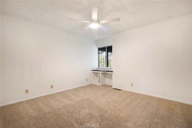 empty room featuring ceiling fan, light colored carpet, and a textured ceiling