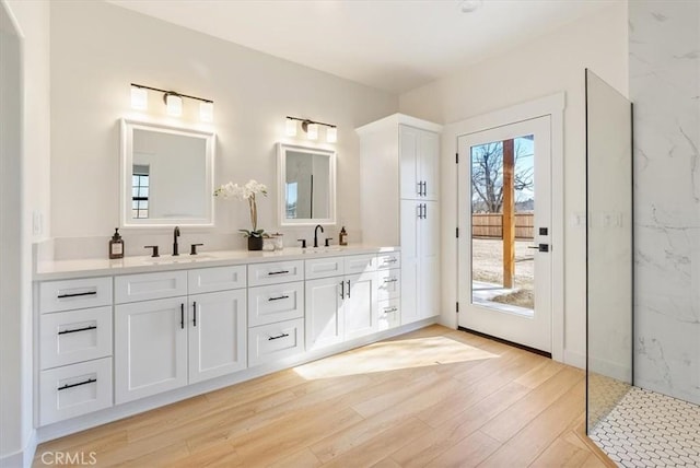 bathroom featuring double vanity, wood finished floors, a marble finish shower, and a sink