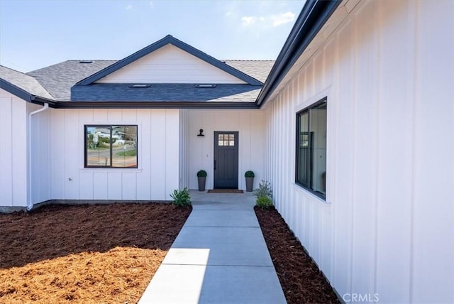 view of exterior entry with board and batten siding and roof with shingles