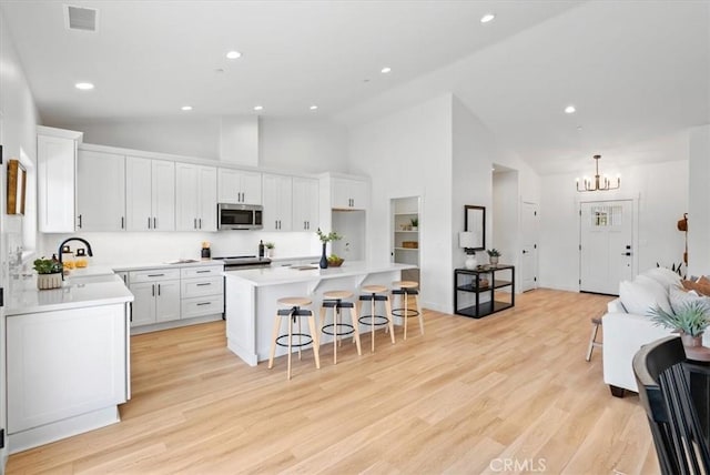 kitchen with visible vents, a sink, stainless steel microwave, a kitchen breakfast bar, and white cabinets