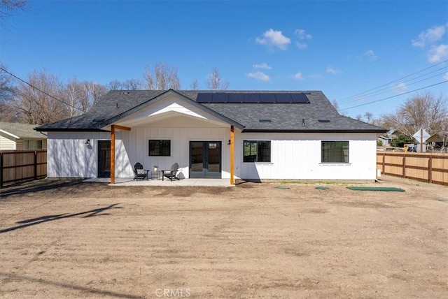 back of property with a patio, french doors, a fenced backyard, and roof mounted solar panels