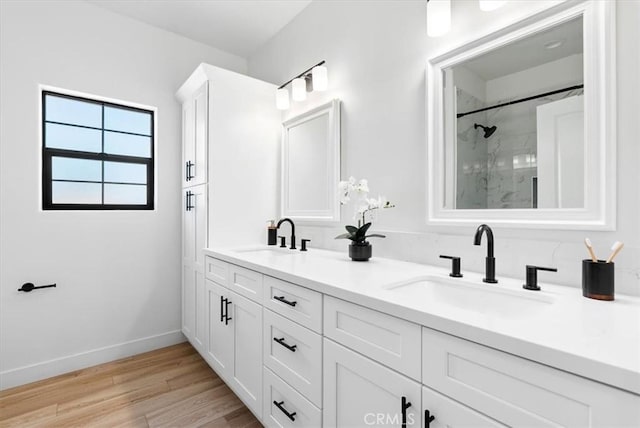 full bathroom featuring a marble finish shower, wood finished floors, baseboards, and a sink