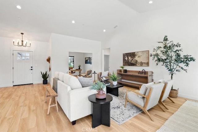 living area featuring a notable chandelier, baseboards, light wood finished floors, and high vaulted ceiling