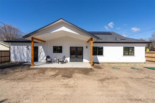 rear view of house with fence, a shingled roof, french doors, a patio area, and roof mounted solar panels