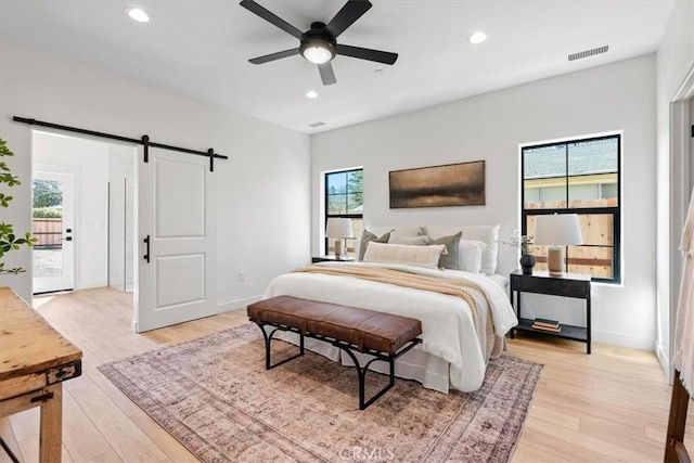 bedroom with light wood-type flooring, a barn door, visible vents, and recessed lighting