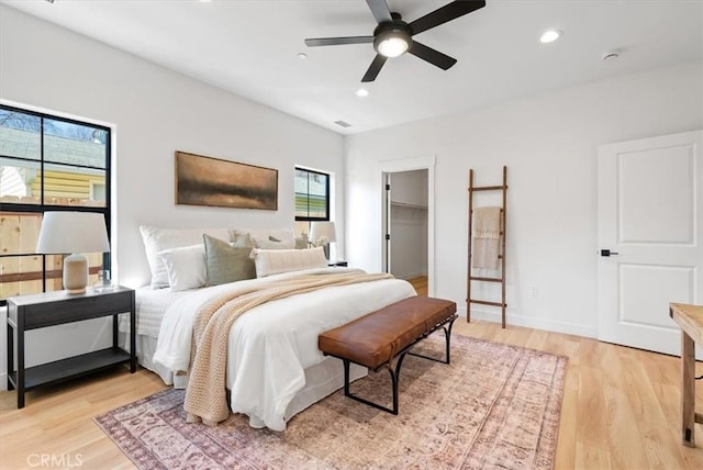 bedroom with light wood finished floors, a walk in closet, baseboards, ceiling fan, and recessed lighting