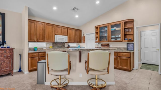 kitchen with lofted ceiling, light tile patterned floors, tasteful backsplash, a kitchen island, and a breakfast bar area