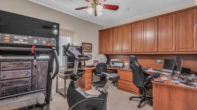 office with built in desk, light colored carpet, and ceiling fan