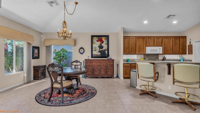 kitchen with an inviting chandelier, hanging light fixtures, light tile patterned floors, light stone countertops, and a breakfast bar area