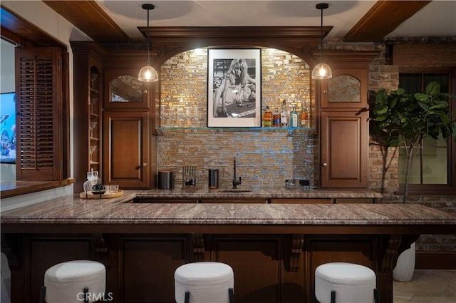 bar with beam ceiling, hanging light fixtures, dark stone counters, and sink