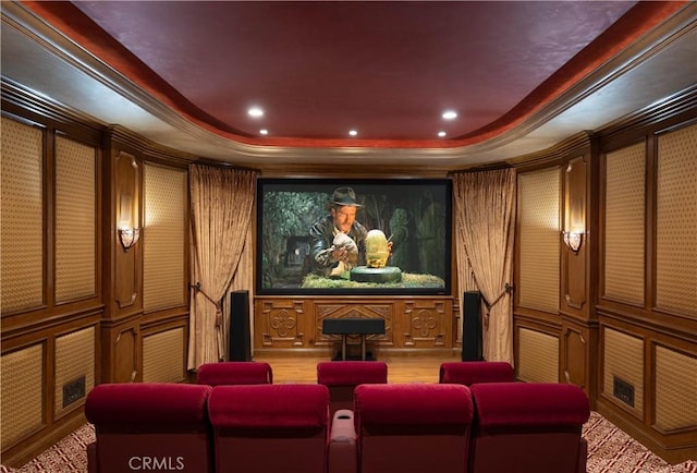 home theater room with a raised ceiling, wood walls, and ornamental molding