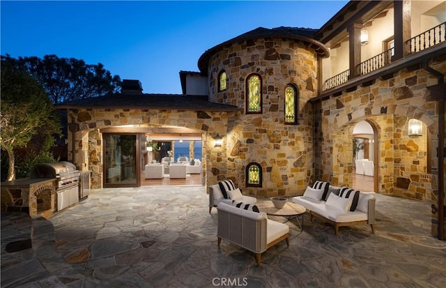 patio terrace at dusk with an outdoor hangout area, a balcony, area for grilling, and a grill