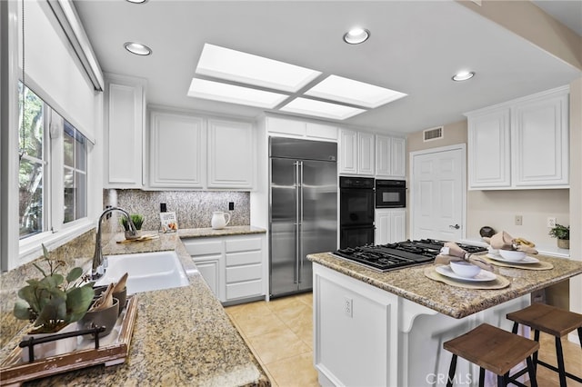 kitchen with white cabinetry, sink, tasteful backsplash, a breakfast bar, and black appliances