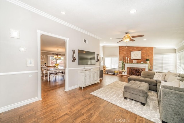 living room with hardwood / wood-style flooring, ceiling fan with notable chandelier, ornamental molding, and a brick fireplace