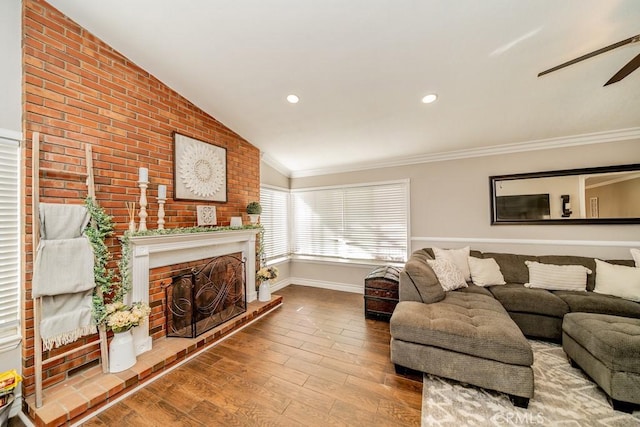 living room with ceiling fan, a brick fireplace, hardwood / wood-style floors, vaulted ceiling, and ornamental molding