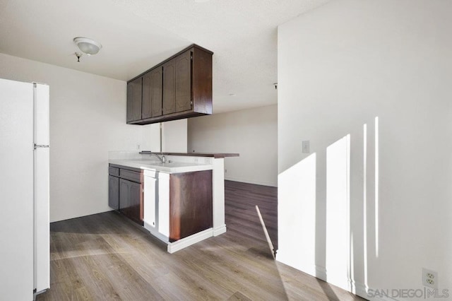 kitchen featuring light wood-type flooring, white refrigerator, kitchen peninsula, and dark brown cabinetry