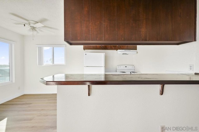 kitchen with a kitchen breakfast bar, light hardwood / wood-style flooring, a healthy amount of sunlight, and white appliances