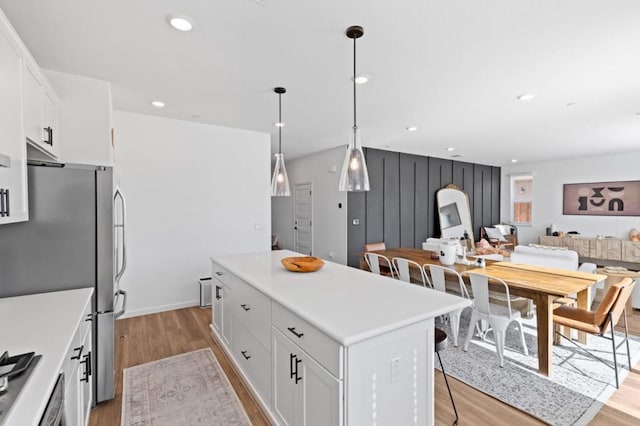 kitchen featuring white cabinetry, light wood-type flooring, stainless steel refrigerator, a kitchen island, and pendant lighting