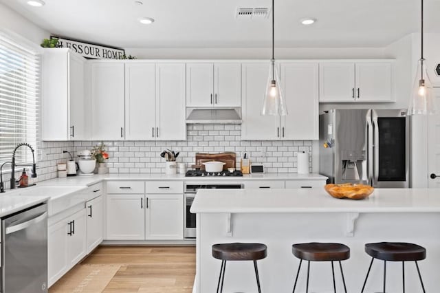 kitchen with white cabinets, a kitchen bar, decorative light fixtures, stainless steel appliances, and sink