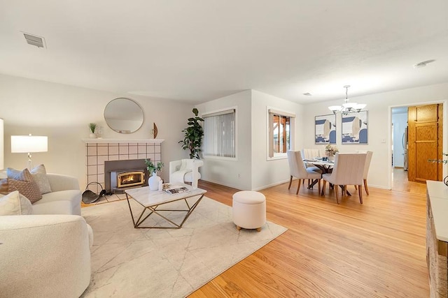 living room featuring a tiled fireplace, light hardwood / wood-style flooring, and a chandelier