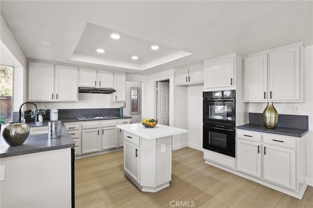 kitchen featuring a center island, a raised ceiling, black double oven, light wood-type flooring, and white cabinetry