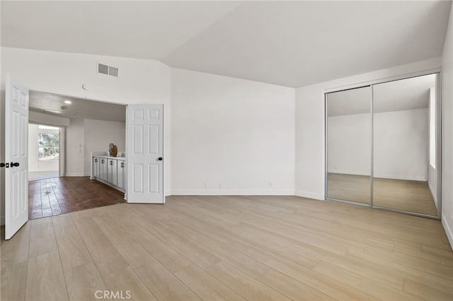 unfurnished bedroom featuring light hardwood / wood-style floors, vaulted ceiling, and a closet