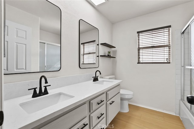 full bathroom featuring bath / shower combo with glass door, vanity, wood-type flooring, and toilet