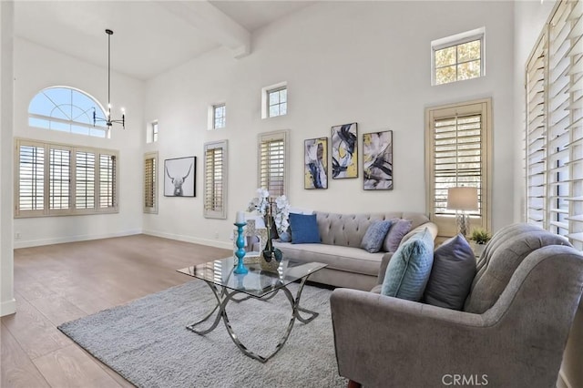 living room featuring light hardwood / wood-style flooring, a towering ceiling, beamed ceiling, and a notable chandelier