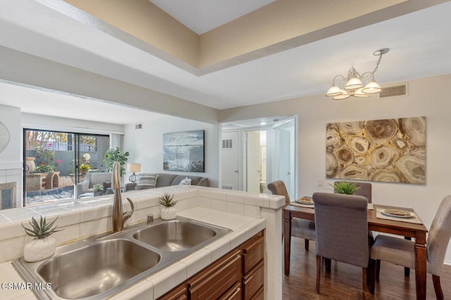 kitchen with sink, hanging light fixtures, dark hardwood / wood-style floors, tile countertops, and a chandelier