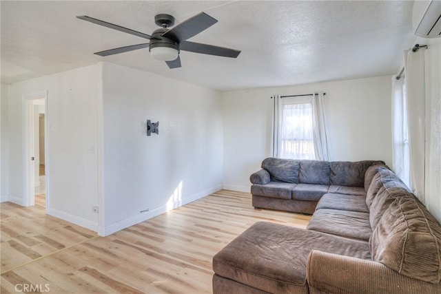 living room with ceiling fan, light hardwood / wood-style floors, an AC wall unit, and a textured ceiling