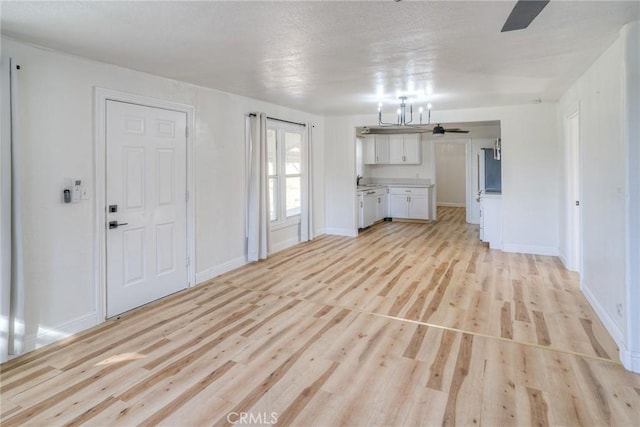 unfurnished living room with ceiling fan with notable chandelier, light wood-type flooring, and sink