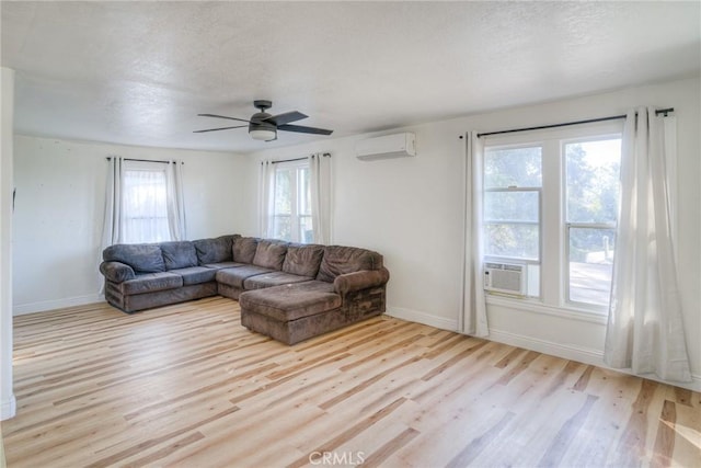 living room with an AC wall unit, ceiling fan, light hardwood / wood-style flooring, and a textured ceiling