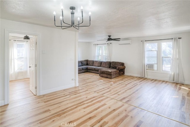 living room featuring a wall unit AC, plenty of natural light, ceiling fan with notable chandelier, and light wood-type flooring