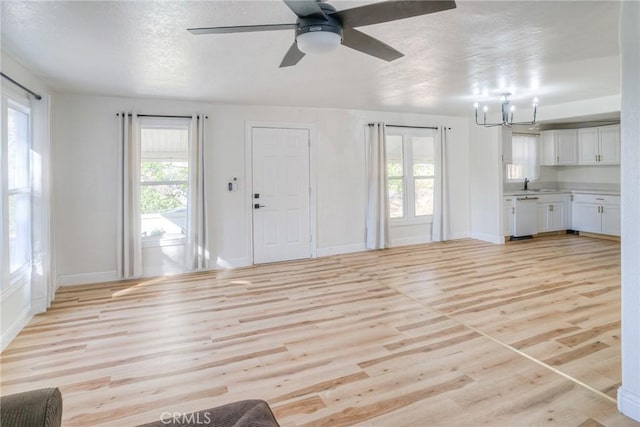 unfurnished living room with ceiling fan with notable chandelier, light wood-type flooring, and plenty of natural light