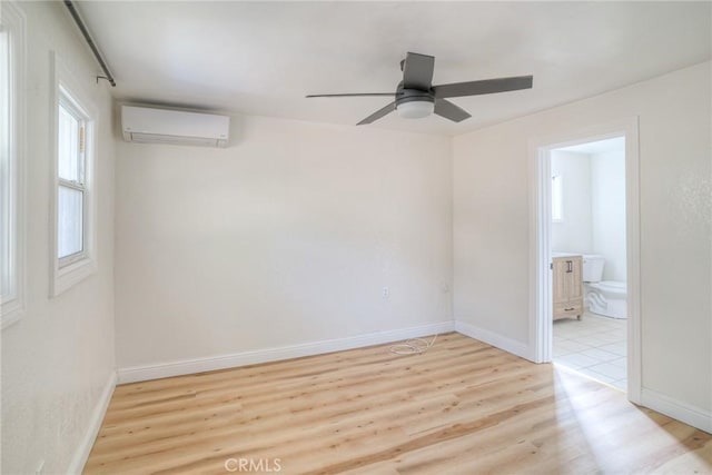 spare room featuring a wall unit AC, ceiling fan, and light hardwood / wood-style floors