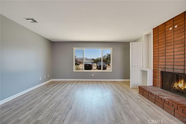 unfurnished living room featuring a brick fireplace and light hardwood / wood-style flooring