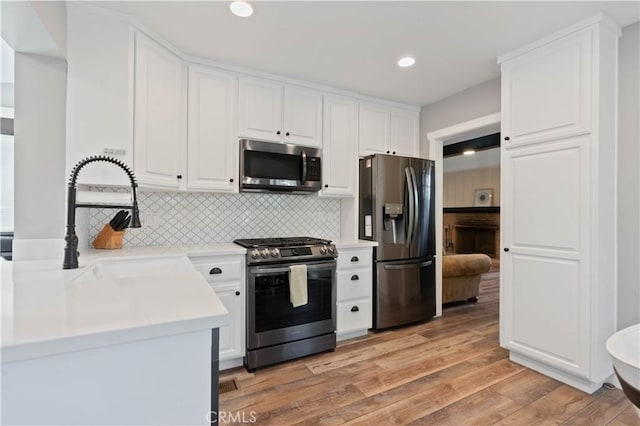 kitchen with white cabinetry, stainless steel appliances, light hardwood / wood-style floors, sink, and backsplash