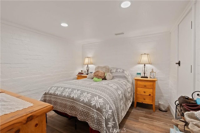 bedroom featuring brick wall, ornamental molding, and hardwood / wood-style floors