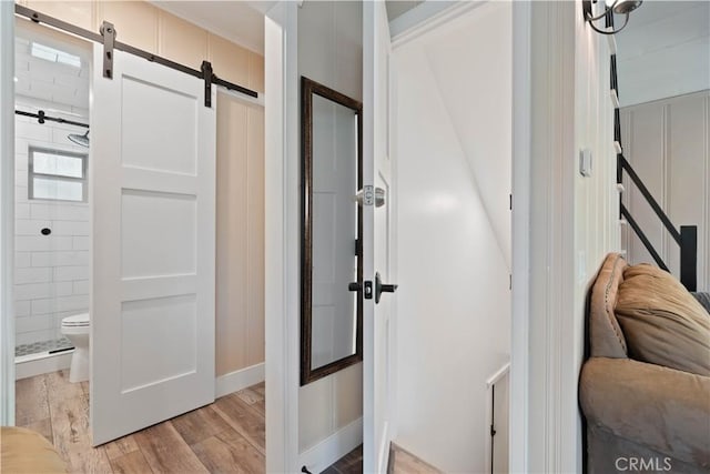 hallway with a barn door, ornamental molding, and light hardwood / wood-style flooring