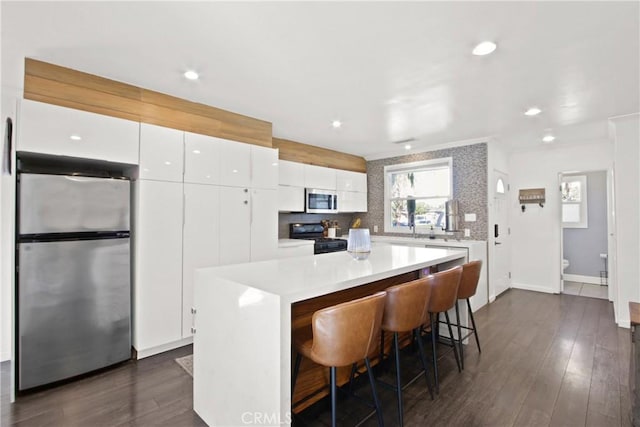 kitchen with dark wood-type flooring, a breakfast bar area, a center island, stainless steel appliances, and white cabinets