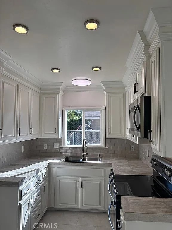 kitchen featuring white cabinetry, electric range, sink, crown molding, and decorative backsplash