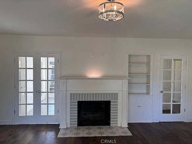 unfurnished living room with a brick fireplace, dark hardwood / wood-style flooring, built in features, and french doors