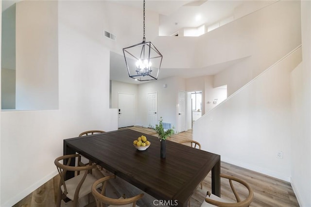 dining area with hardwood / wood-style floors, a notable chandelier, a towering ceiling, and a wealth of natural light