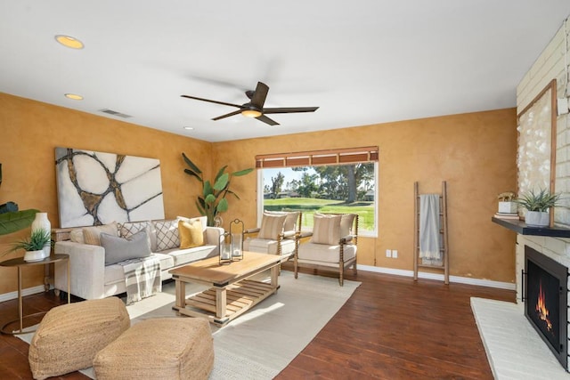 living room with a brick fireplace, dark hardwood / wood-style floors, and ceiling fan